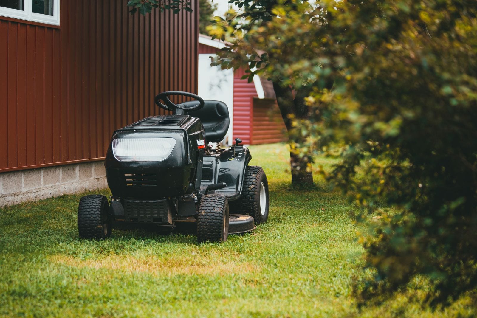Sort havetraktor parkeret på græsplæne ved en rød lade